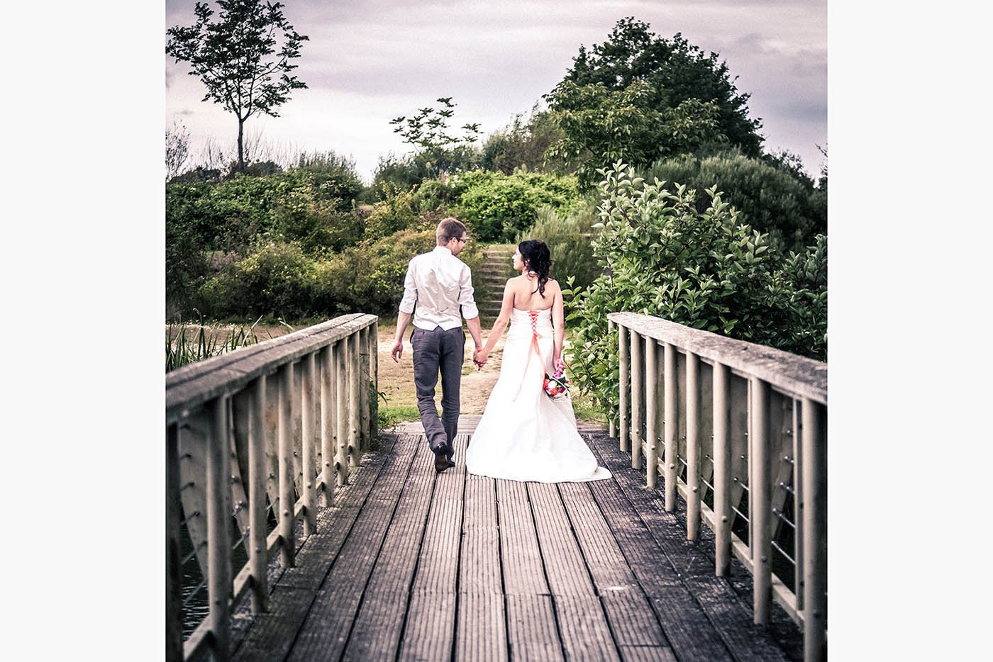 Un couple de mariés main dans la main traversant un pont en bois en Vendée